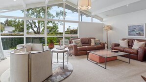 A spacious living room with a large window, leather sofas, a coffee table, and a lamp. - Spacious family home in Meadowbank| by Furnished Rentals (Auckland)
