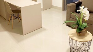 A modern living room with a white desk, a beige sofa, and a round coffee table with a flower vase. - Fortune by Day by Day (Joao Pessoa)