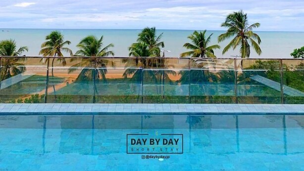 A clear view of a swimming pool with a 'DAY BY DAY SHORT STAY' sign, palm trees, and a beach in the background. - Fortune by Day by Day (Joao Pessoa)