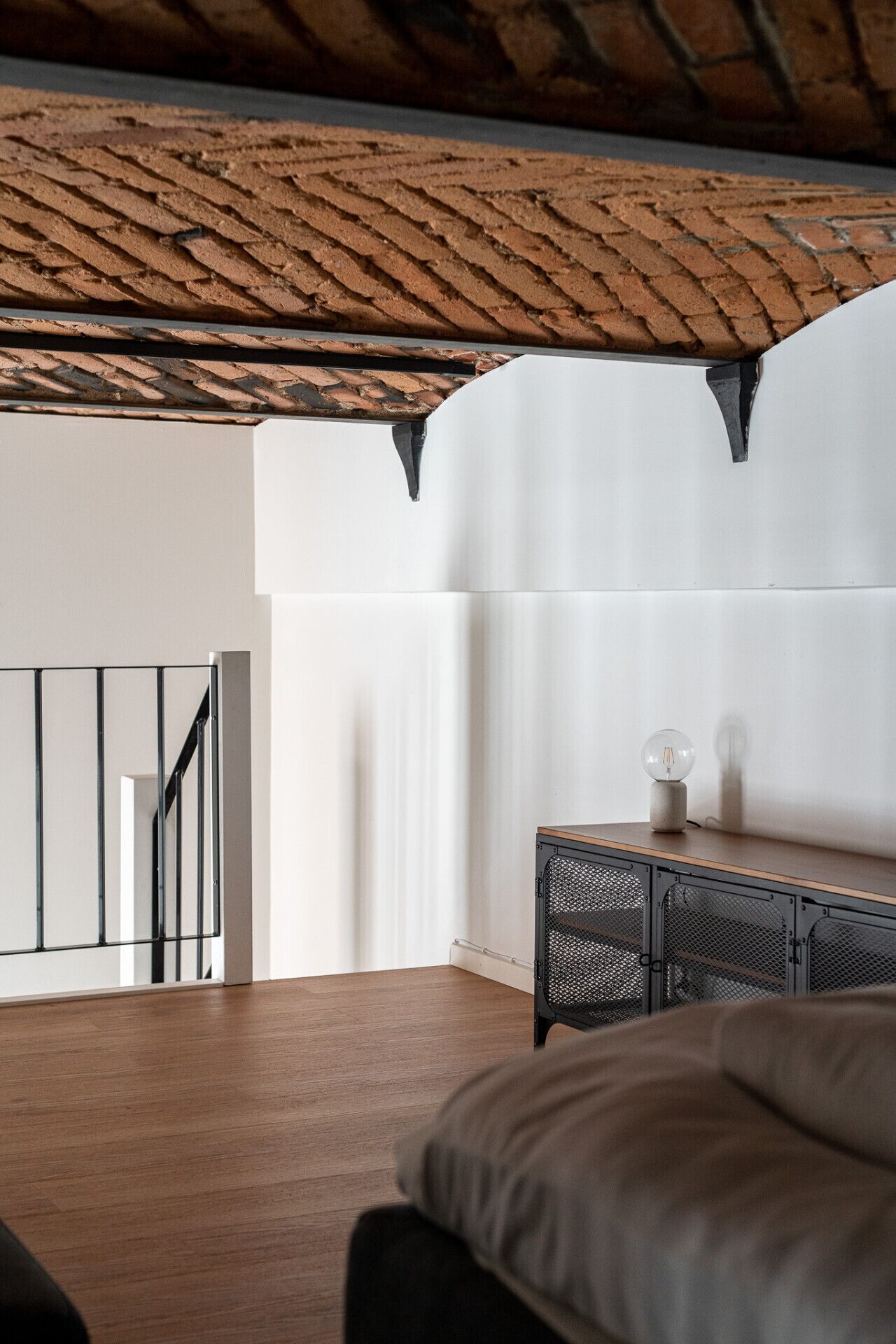 A modern room with a wooden ceiling, a staircase, a white wall, and a metal cabinet with a light bulb.