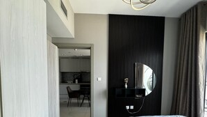 A modern hotel room with a large bed, a desk, and a kitchenette in the background. - 1BHK in Business Bay close to metro  (Dubai)