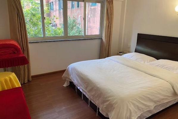 A bedroom with a bed, a window with curtains, and a view of greenery outside.