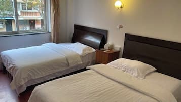 A hotel room with two beds, a window, a nightstand, and a wall-mounted light.