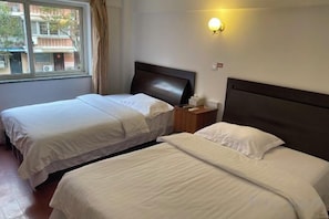 Habitación de hotel con dos camas, una ventana, una mesita de noche y una lámpara fijada a la pared.
