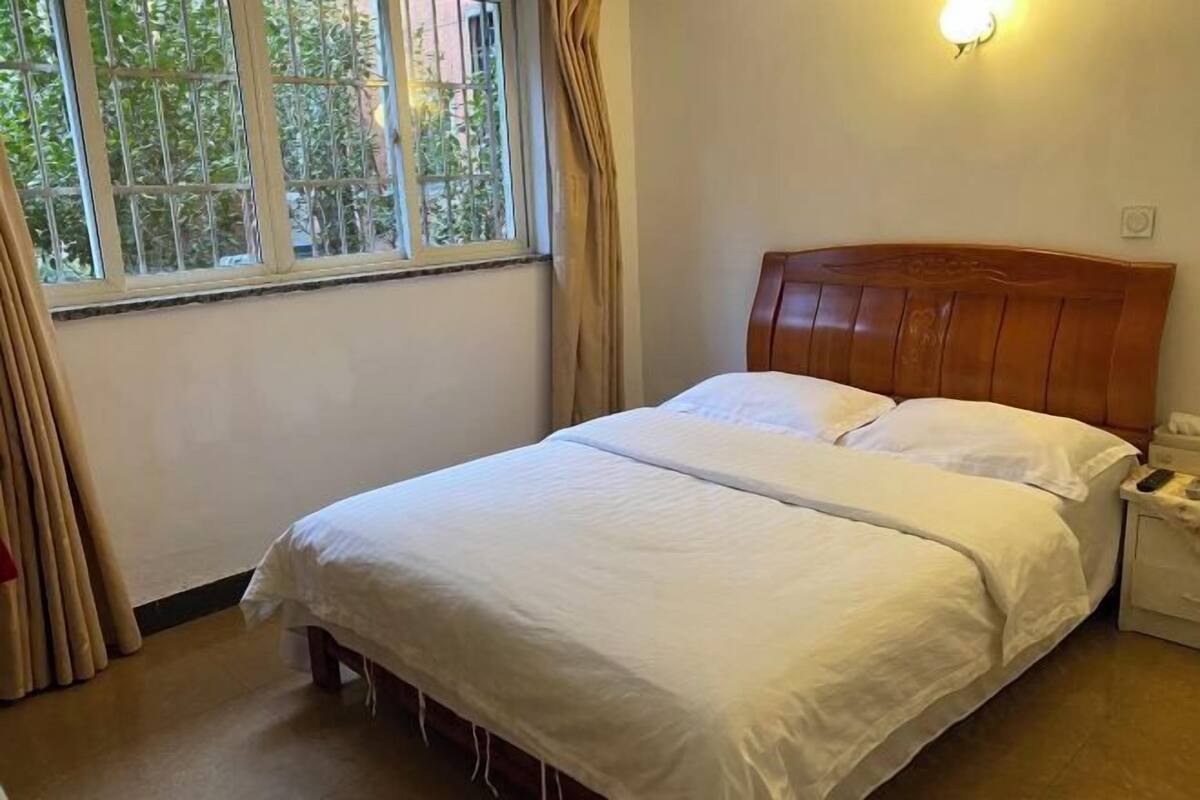 A single bed with a wooden headboard in a room with a window and a nightstand.