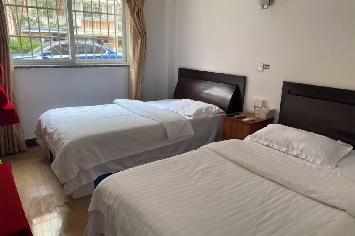 A hotel room with two beds, a TV, a nightstand, and a window with a view of the street.