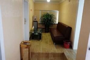 En hall med en brun lädersoffa, ett litet bord, en krukväxt och en röd papperskorg.