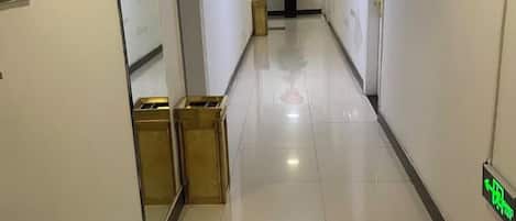A corridor with a reflective floor, a trash bin, and a potted plant.