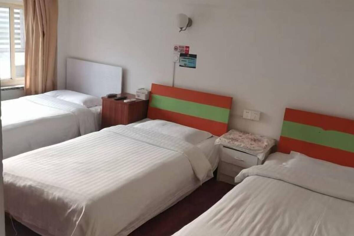 A hotel room with two beds, a nightstand, a wall-mounted light, and a window with curtains.