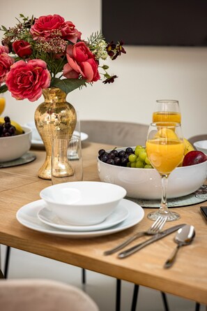 A breakfast setting with a fruit bowl, a glass of orange juice, a vase of flowers, and dining utensils on a wooden table. - 3-bdr Stunning LUX Villa Parking Central London (London)