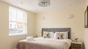 A bedroom with a large bed, a bedside table, a window with blinds, and a wall-mounted light fixture. - 3-bdr Stunning LUX Villa Parking Central London (London)