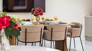 A dining area with a table set for four, featuring a vase of flowers, fruit, and glasses of orange juice. - 3-bdr Stunning LUX Villa Parking Central London (London)