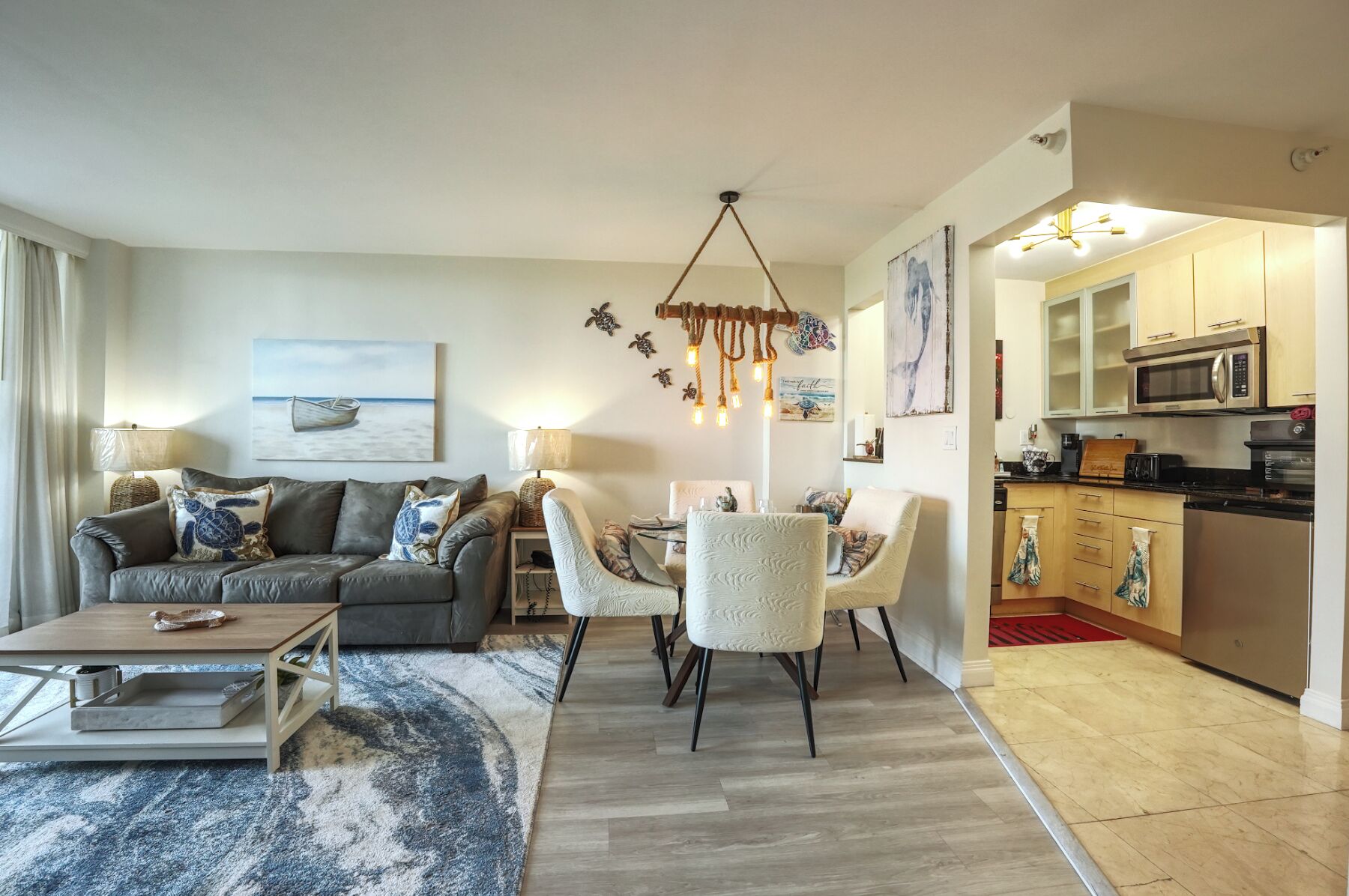 Un salon moderne comprenant un canapé, une table basse et un coin repas. La cuisine est équipée d’un four à micro-ondes et de placards.