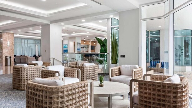 A modern lobby with wicker furniture, a central round table, and a glass wall offering a view of the interior. - Turtle Cove (Fort Lauderdale)