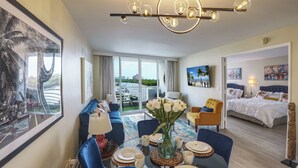 A modern hotel room with a dining area, a large window with a view of the city, and a separate bedroom with a bed and artwork. - Turtle Cove (Fort Lauderdale)