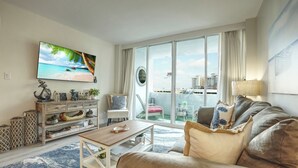 A spacious living room with a large TV, a comfortable sofa, a coffee table, and a balcony with a view of the city. - Turtle Cove (Fort Lauderdale)