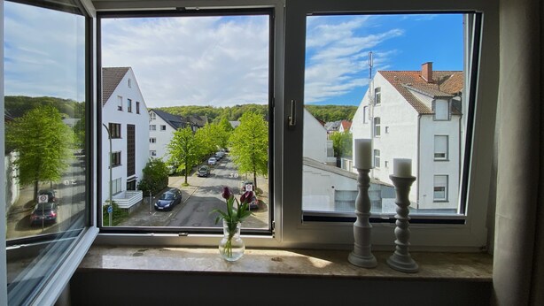 A window with a view of a residential street, a vase with flowers, and two candle holders on the windowsill. - Cozy apartment /Central and comfortable / Only 20 min walk from the zoo (Osnabrück)