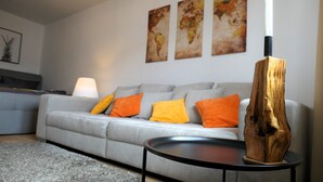 A modern living room with a grey sofa, orange cushions, a round black coffee table, and a wooden sculpture. - Cozy apartment /Central and comfortable / Only 20 min walk from the zoo (Osnabrück)