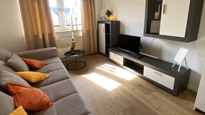 A modern living room with a grey sofa, a TV, and a small table with a candle. - Cozy apartment /Central and comfortable / Only 20 min walk from the zoo (Osnabrück)