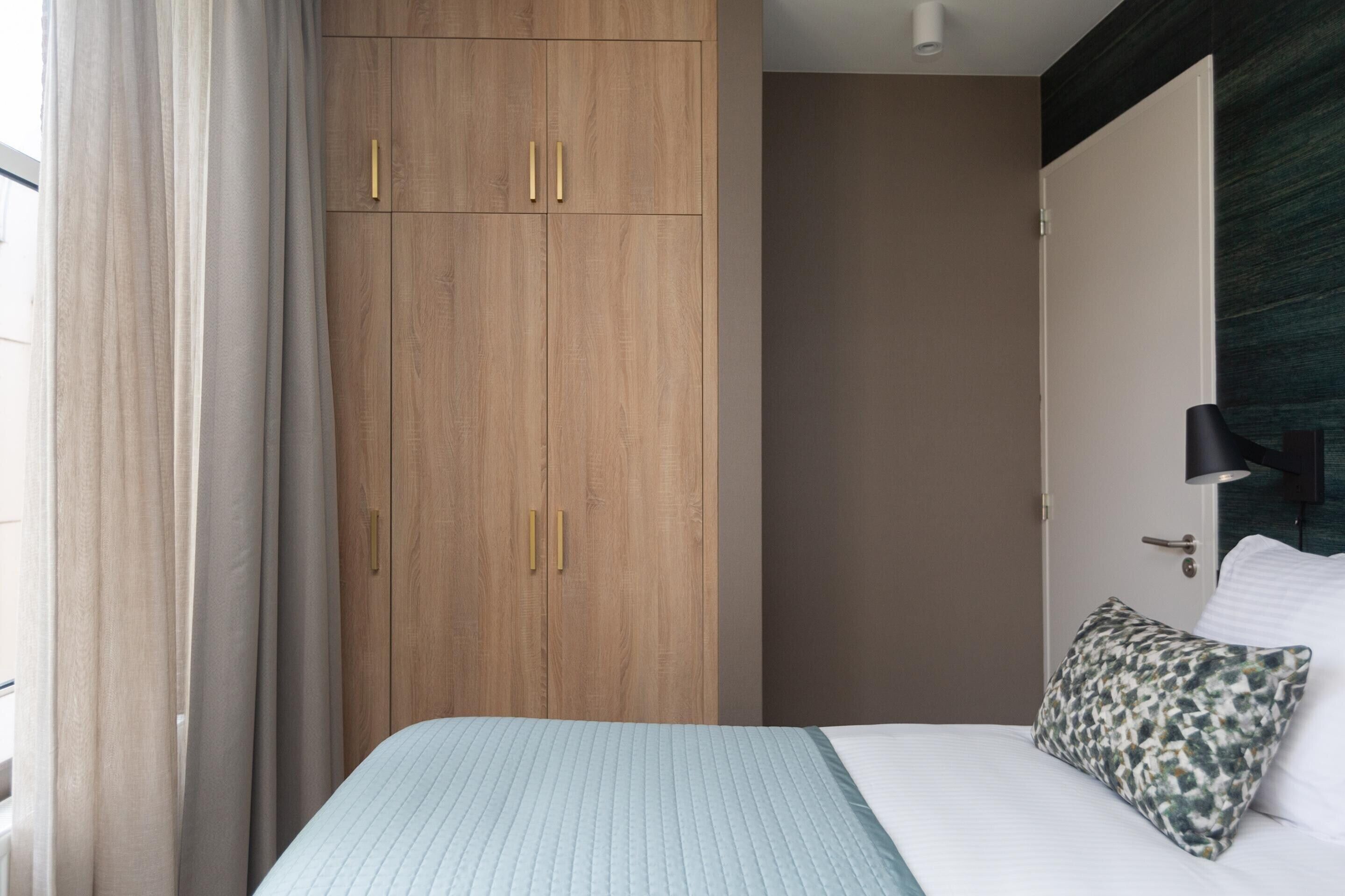 A bedroom with a bed, a wardrobe, a door, and a nightstand with a lamp.