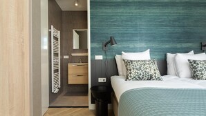 A modern hotel room with a bed, bedside table, lamp, and a view into the bathroom. - Stylish 2-bedroom Apartment in The Hague (The Hague)