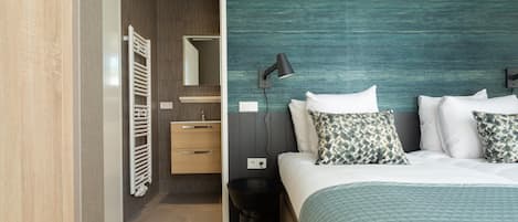 A modern hotel room with a bed, bedside table, lamp, and a view into the bathroom.