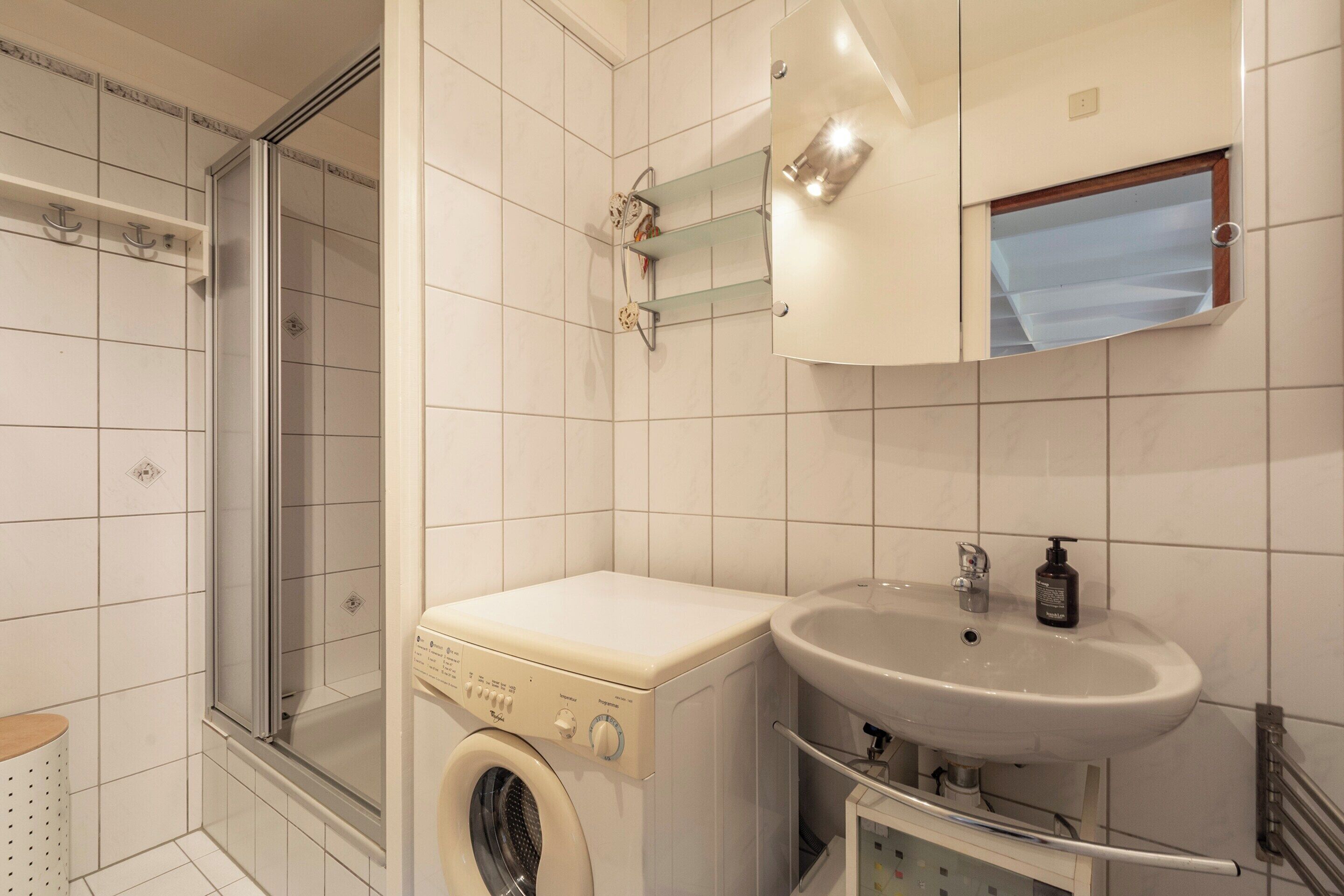 A bathroom with a washing machine, a sink, and a glass shower enclosure.