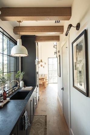 A modern kitchen with a large window, a pendant light, and a wooden beam ceiling.