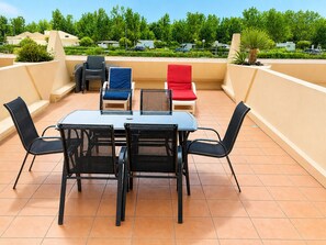 Una terraza en la azotea con una mesa, sillas, un pequeño sofá y una planta en maceta.