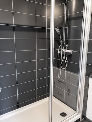 A glass-enclosed shower with a handheld showerhead and a control panel.