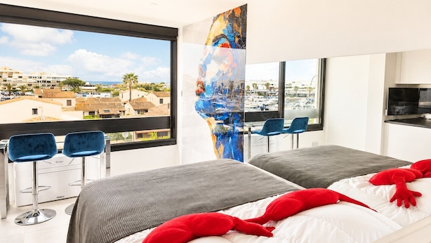 Een moderne hotelkamer met twee bedden, een groot raam met uitzicht op de stad, een schilderij aan de muur en een televisie.