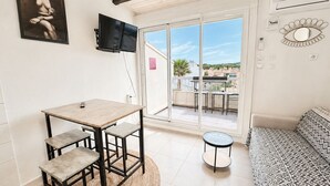 A room with a table, chairs, a sofa, a TV, a window, and a balcony with a table and chairs. - Naturiste Cap d'Agde Port Soleil 479 (Cap d'agde)