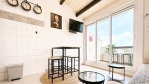 A room with a tiled floor, a television mounted on the wall, a balcony with a railing, and a window with a view of the outside. - Naturiste Cap d'Agde Port Soleil 479 (Cap d'agde)