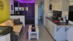Un espacio habitable compacto con kitchenette, un sofá, una pequeña mesa de centro y una mesa de comedor.
