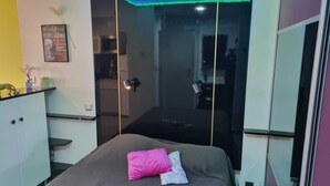 Un dormitorio con cama, mesita de noche, espejo y una puerta con panel de vidrio.