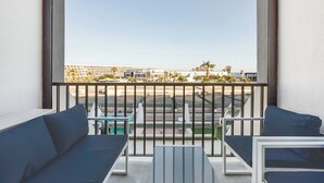 Un balcón con vistas a palmeras y edificios, amoblado con un sofá y una mesa.