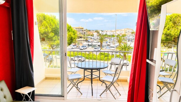 Een balkon met een tafel en stoelen, een bank en een televisiescherm.