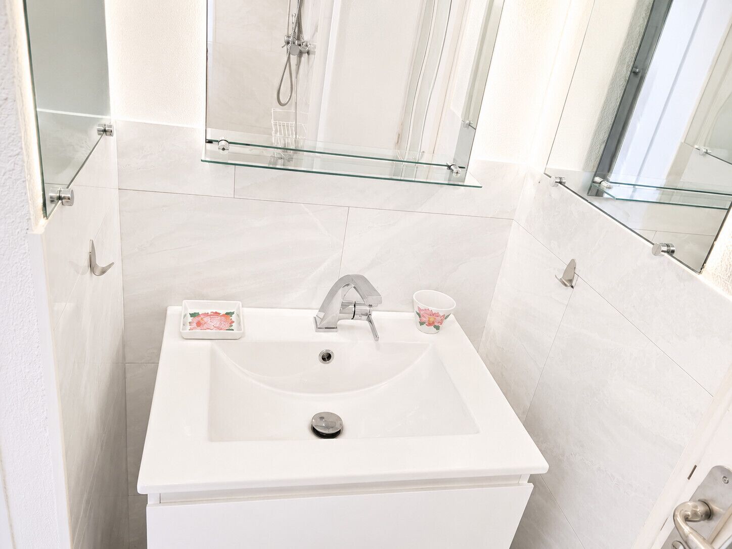A bathroom with a white sink, a glass shelf above it, and a glass shower enclosure.