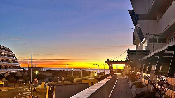 A modern building with a flat roof and a long, narrow balcony overlooking a body of water during sunset. - Naturiste Cap d'Agde Phantasme Naturiste Port Nature 94 Vue Mer (Agde)