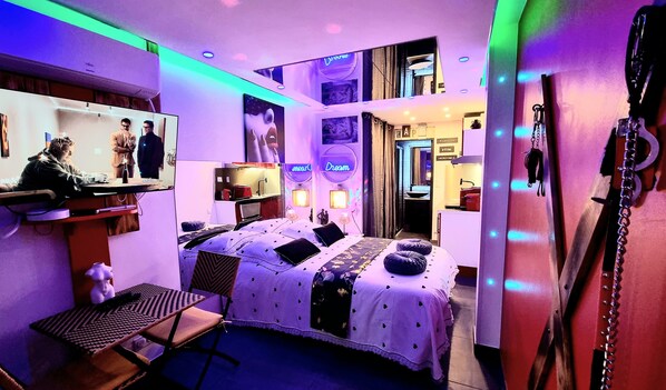 Habitación de hotel compacta con cama, escritorio y silla. Incluye luces fijadas a la pared y un espejo.