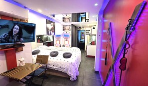 Moderni hotellihuone, jossa on sänky, televisio, työpöytä ja taustalla näkyy kylpyhuone.