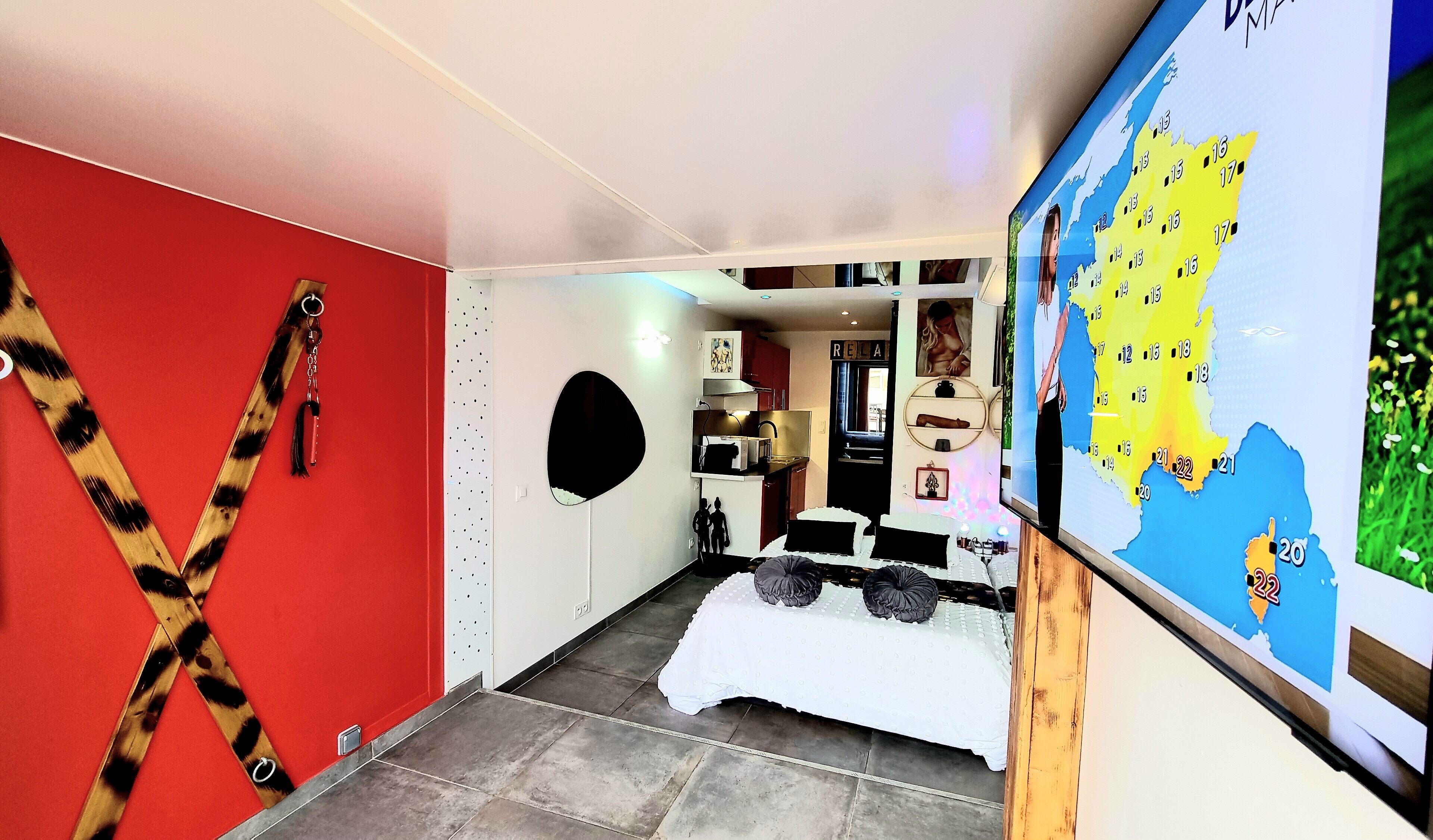 Une chambre d’hôtel avec un mur rouge, un lit recouvert d’une courtepointe blanche, une carte accrochée au mur et un petit coin cuisine.