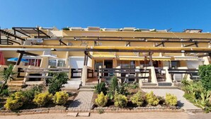 A hotel with multiple balconies, a central entrance, and a landscaped garden area.