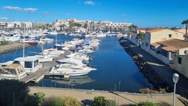 Un port de plaisance où de nombreux bateaux sont amarrés le long d’un canal étroit, entouré de bâtiments et de palmiers.