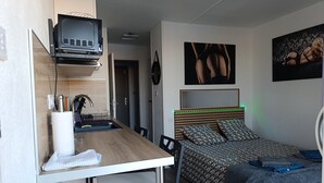 Une chambre à coucher de taille réduite, comprenant un lit, un bureau avec une chaise, un téléviseur et une porte donnant sur la salle de bain.