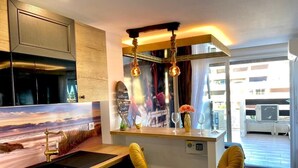 A modern kitchen with a wooden countertop, a built-in sink, and a bar area with stools. There is a decorative wall with a landscape painting and a window with curtains. - Naturiste Cap d'Agde Port Nature 90 (Agde)