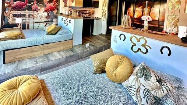 A multi-level living space with a large mirror, a sofa with patterned cushions, and a decorative wall with a floral design. - Naturiste Cap d'Agde Port Nature 90 (Agde)