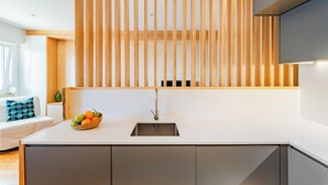 Una cucina moderna con un piano di lavoro bianco, un lavello in acciaio inossidabile e una finestra a listelli in legno.