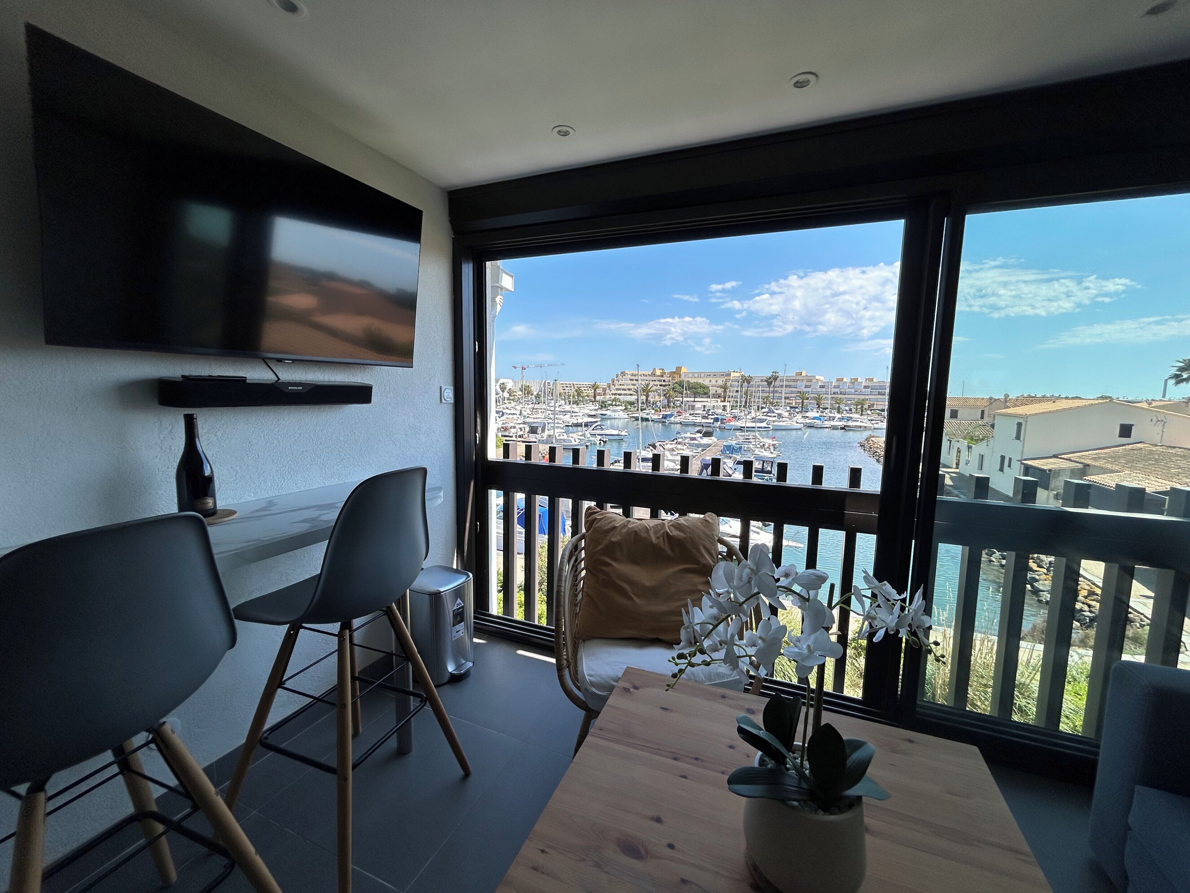 A modern living room with a TV, seating, and a view of a marina.