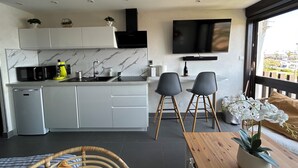 A modern kitchen with a built-in microwave, coffee maker, and sink. There are two chairs and a small table with a potted orchid. A TV is mounted on the wall above the kitchen. - Naturiste Cap d'Agde Port Vénus 212 (Agde)